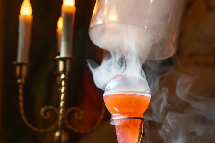 Smoky cocktail in a glass cone with candles in the background.
