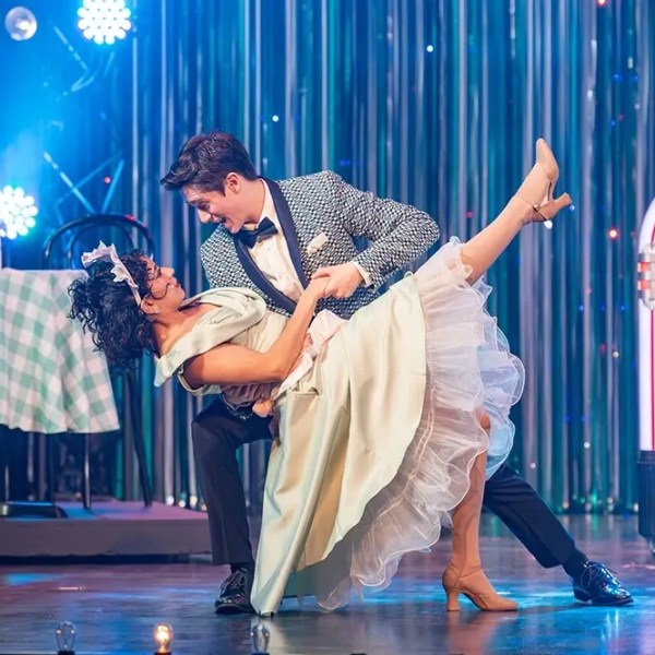 Couple in 1950s attire dancing with jukebox and table in background.