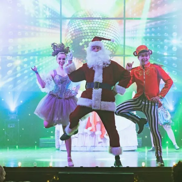 Santa and dancers perform onstage with bright lights and costumes.