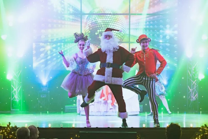 Santa and dancers perform onstage with bright lights and costumes.