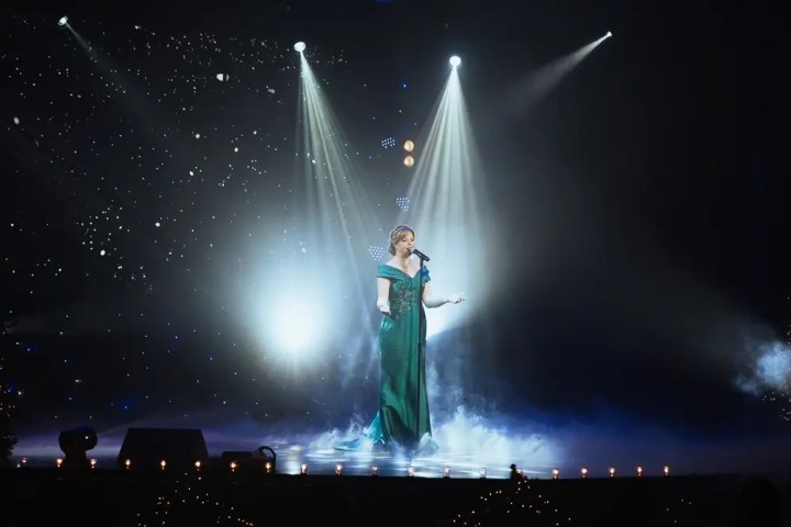 Singer in green dress performs on stage with spotlights and mist.