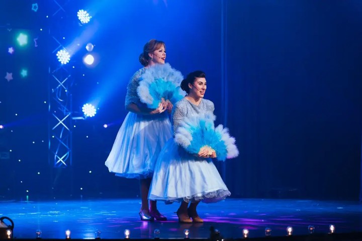 Two performers in blue dresses with feather fans on a stage with blue lighting and star decorations.