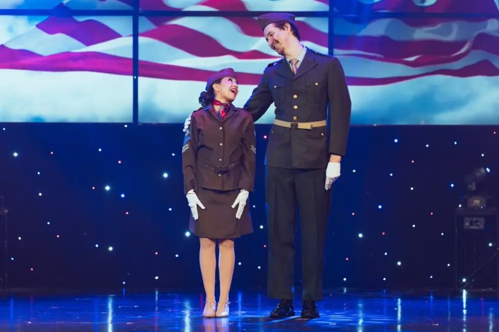 Two performers in vintage uniforms on stage with a flag backdrop.