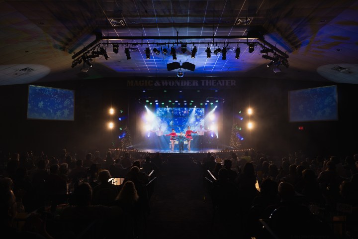 Stage performance with colorful lights at Magic & Wonder Theater, audience visible in darkened seats.