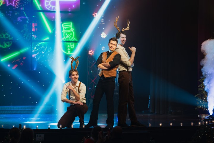 Three men on stage with antlers, Christmas lights and smoke background.