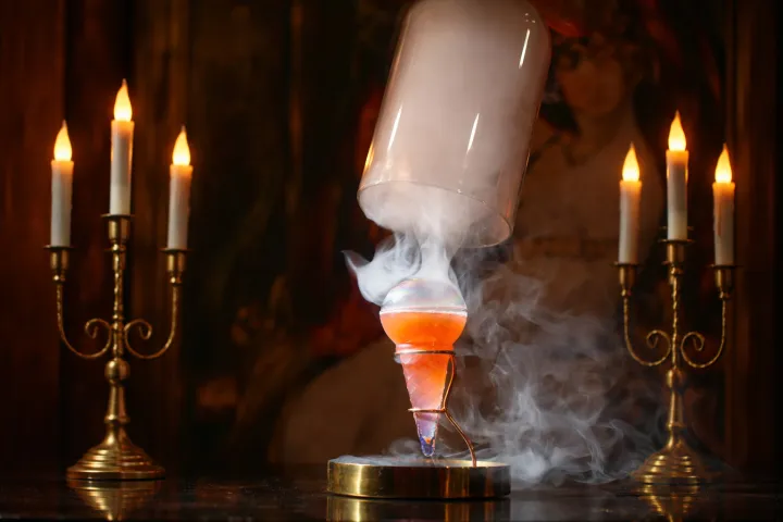 Two candelabras and a smoking cocktail glass under a glass dome on a table.
