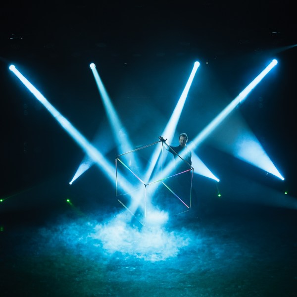 Performer with glowing cube and smoke, surrounded by blue spotlights.