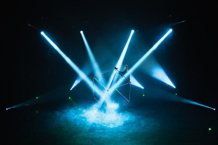 Performer with glowing cube and smoke, surrounded by blue spotlights.