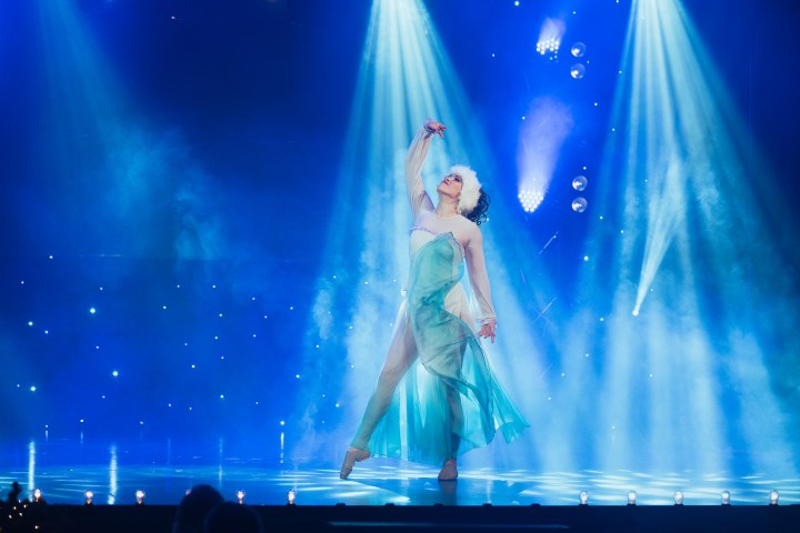 Ballet dancer in a flowing dress performs under bright stage lights.