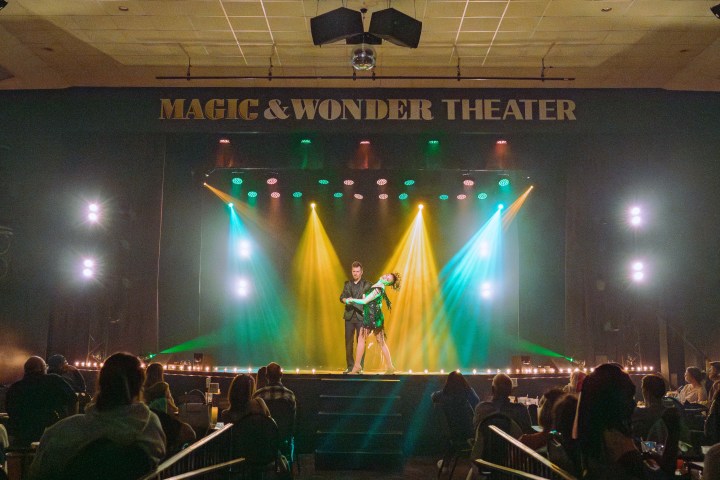 Performer on stage at Magic & Wonder Theater with colorful lights on a cheering audience.