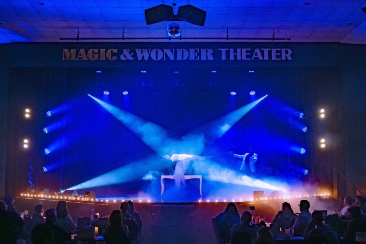 Theater stage with performer levitating in blue light, audience watching.