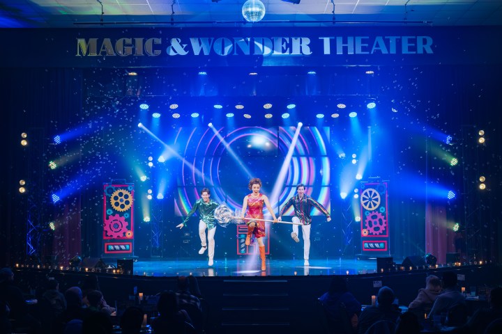 Three performers on a vibrant stage at Magic & Wonder Theater with colorful lights and spotlight effects.