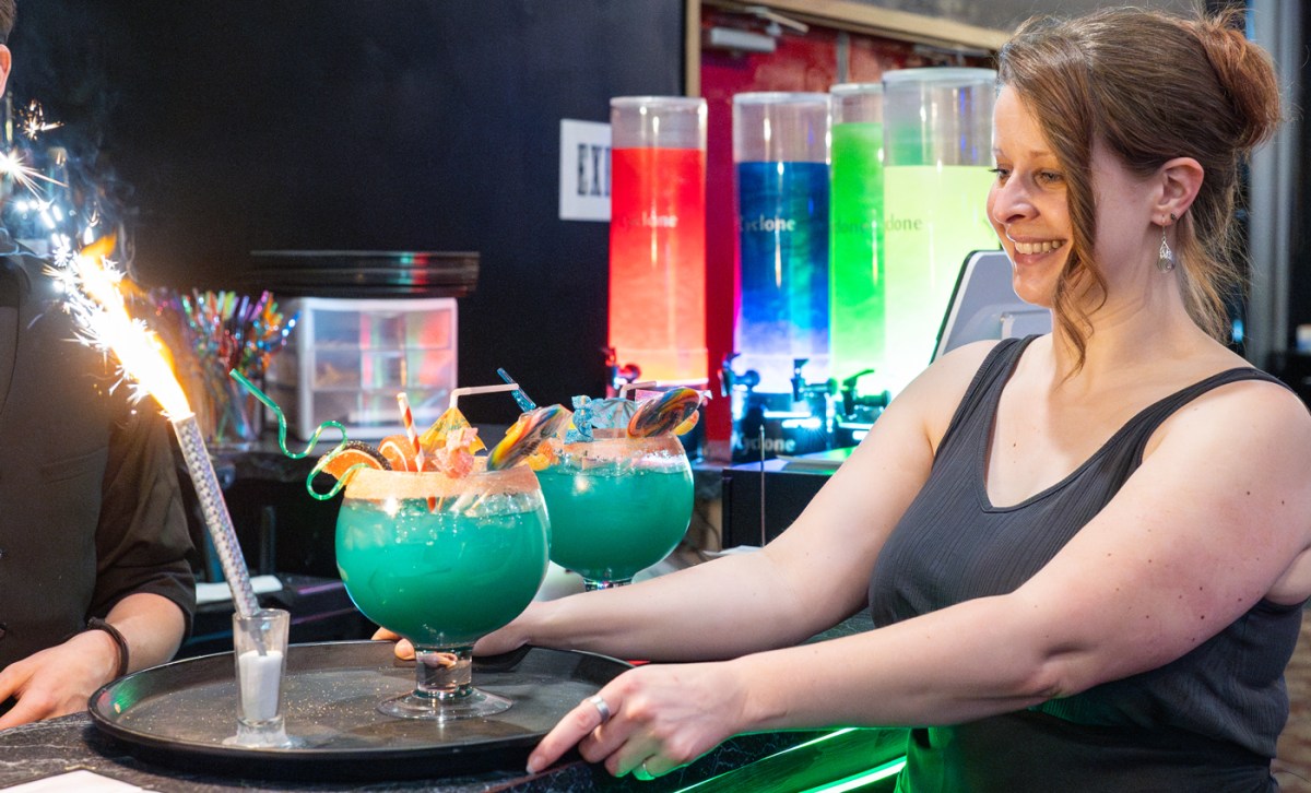 Woman holding tray with large blue cocktails and sparklers at a bar.