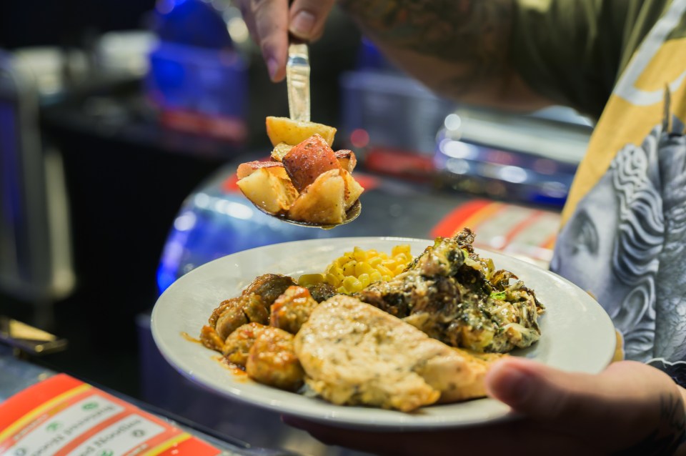 Person serving plate with chicken, corn, potatoes, and greens.