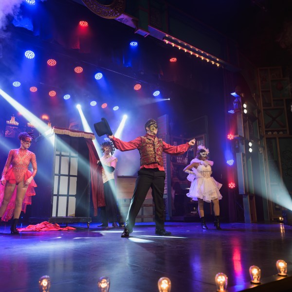 Performers in costumes on a stage with bright lights and smoke effects.