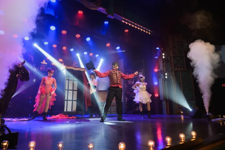 Performers in costumes on a stage with bright lights and smoke effects.
