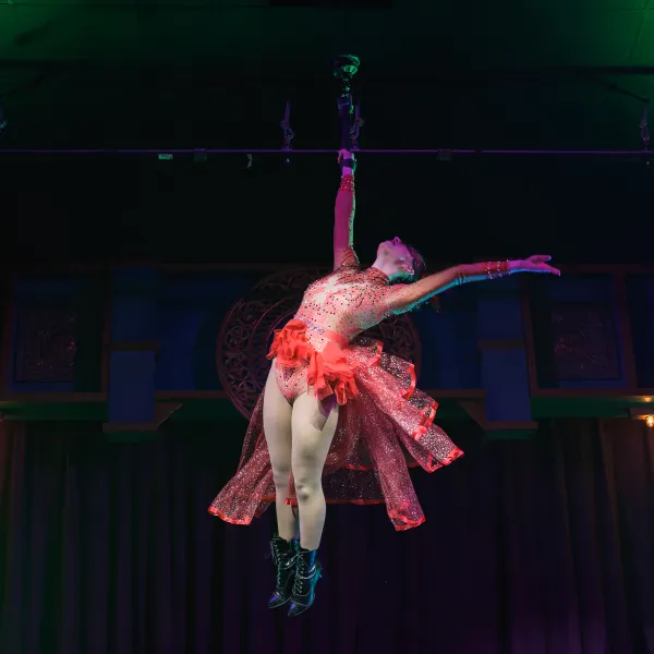 Performer in red costume suspended mid-air on a stage.