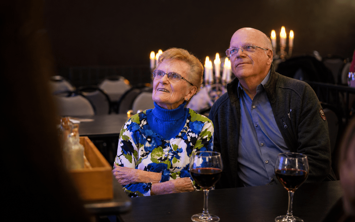 Elderly couple sitting together at a table with wine glasses.