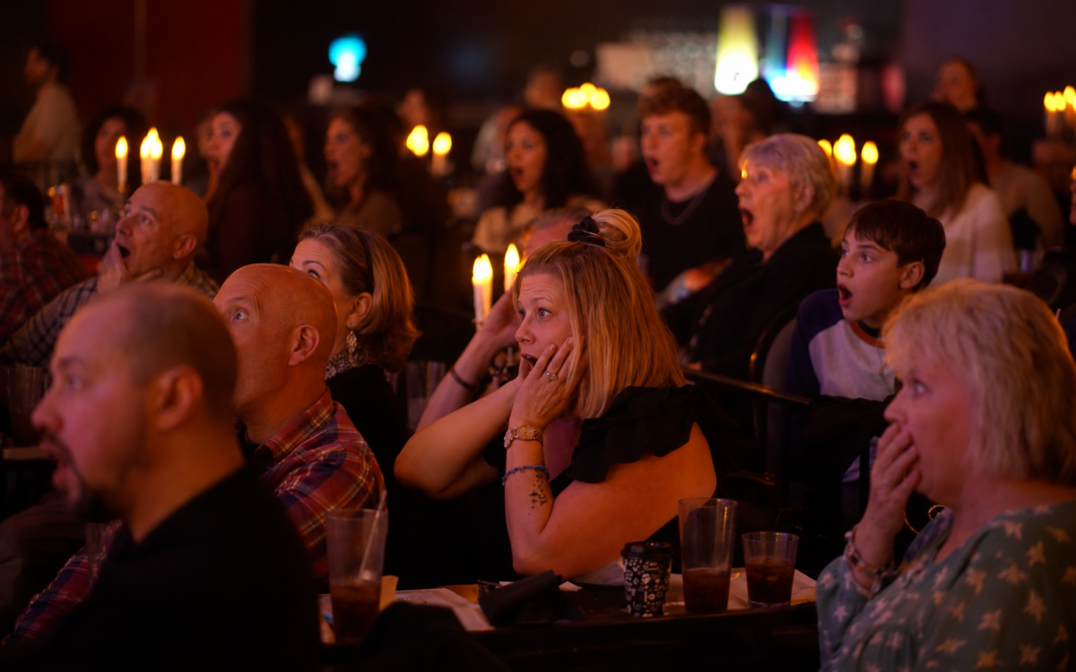 Audience reacts with shock and surprise at an event in a dimly lit room with candles.