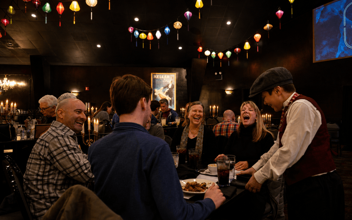 People dining and laughing in dimly lit restaurant with colorful hanging lights.