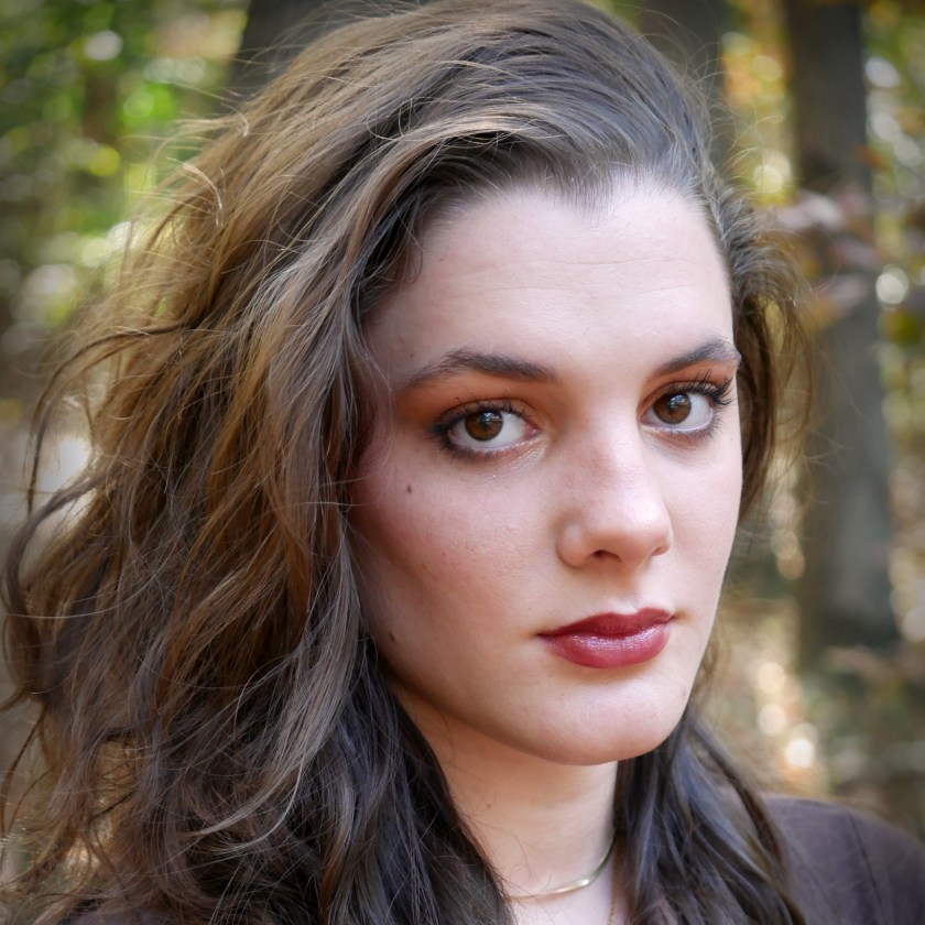 Woman with long hair in forest, looking at camera.