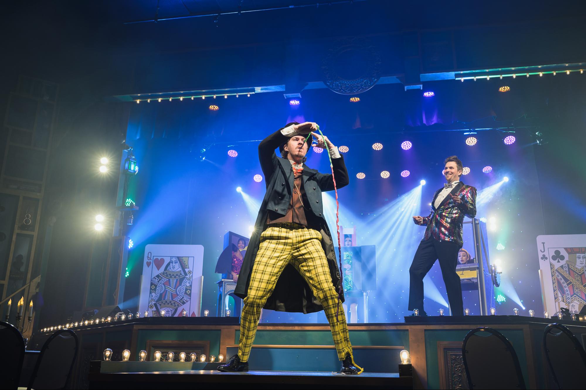 Two performers on stage with bright lights, one holding a microphone.