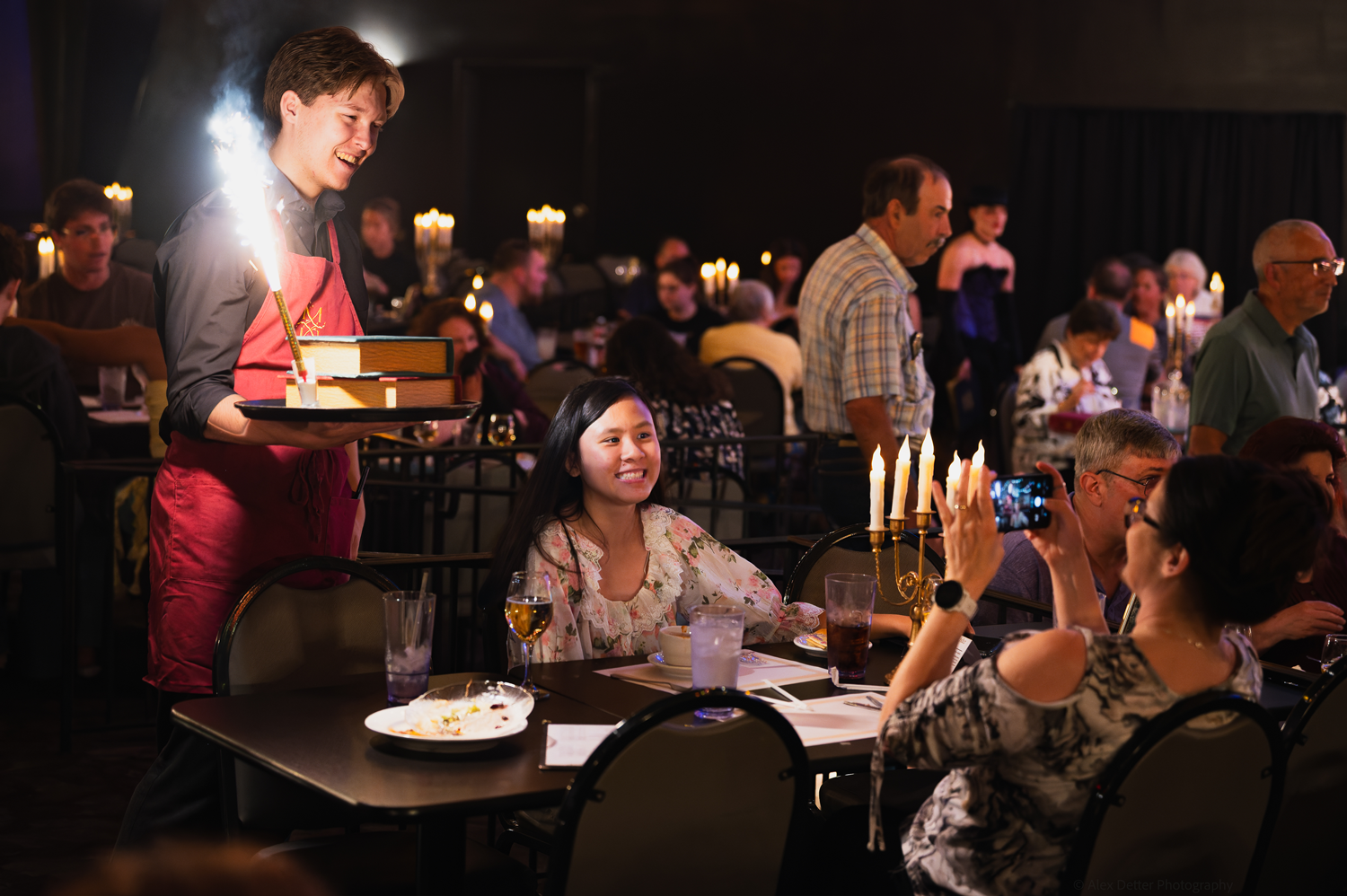 Waiter serves sparkling dessert to happy diner in a dimly lit restaurant.