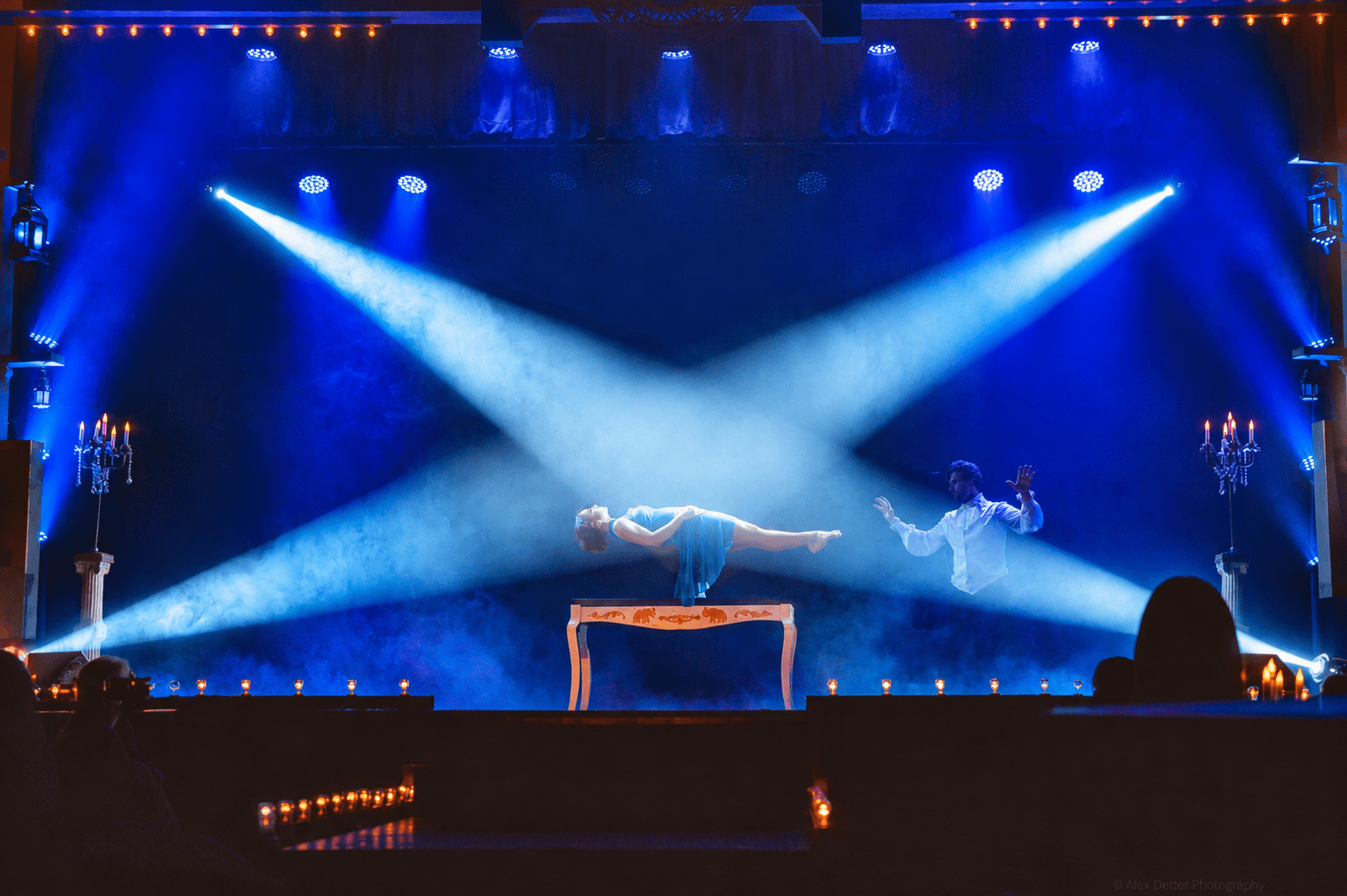 Performer levitating a woman on stage with dramatic lighting.